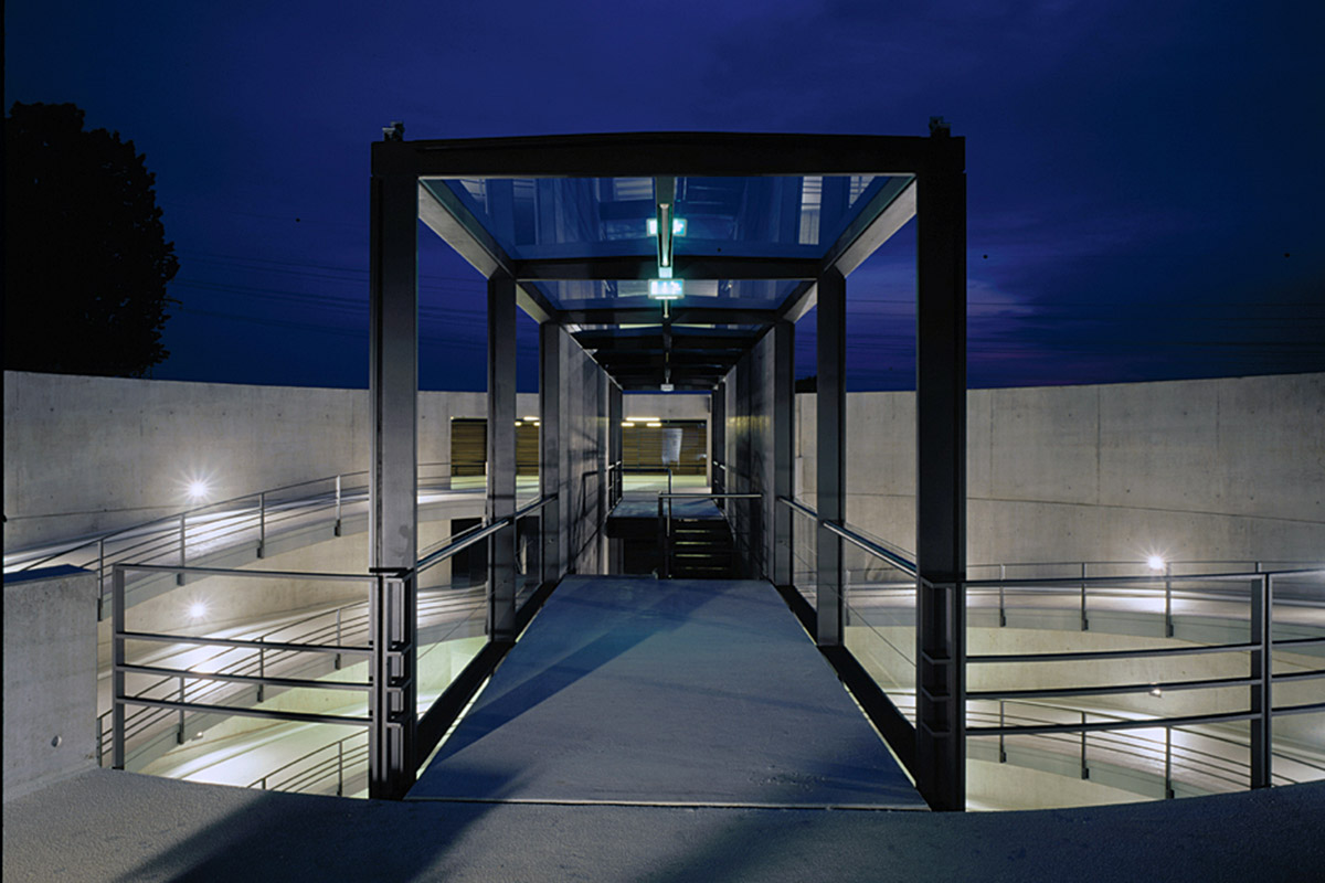 Burda Parkhaus, Offenburg - Parkhaus am Abend in der Mitte mit gläsernem Durchgang und Lichtpunkten an den äußeren Ringwänden - TROPP LIGHTING DESIGN